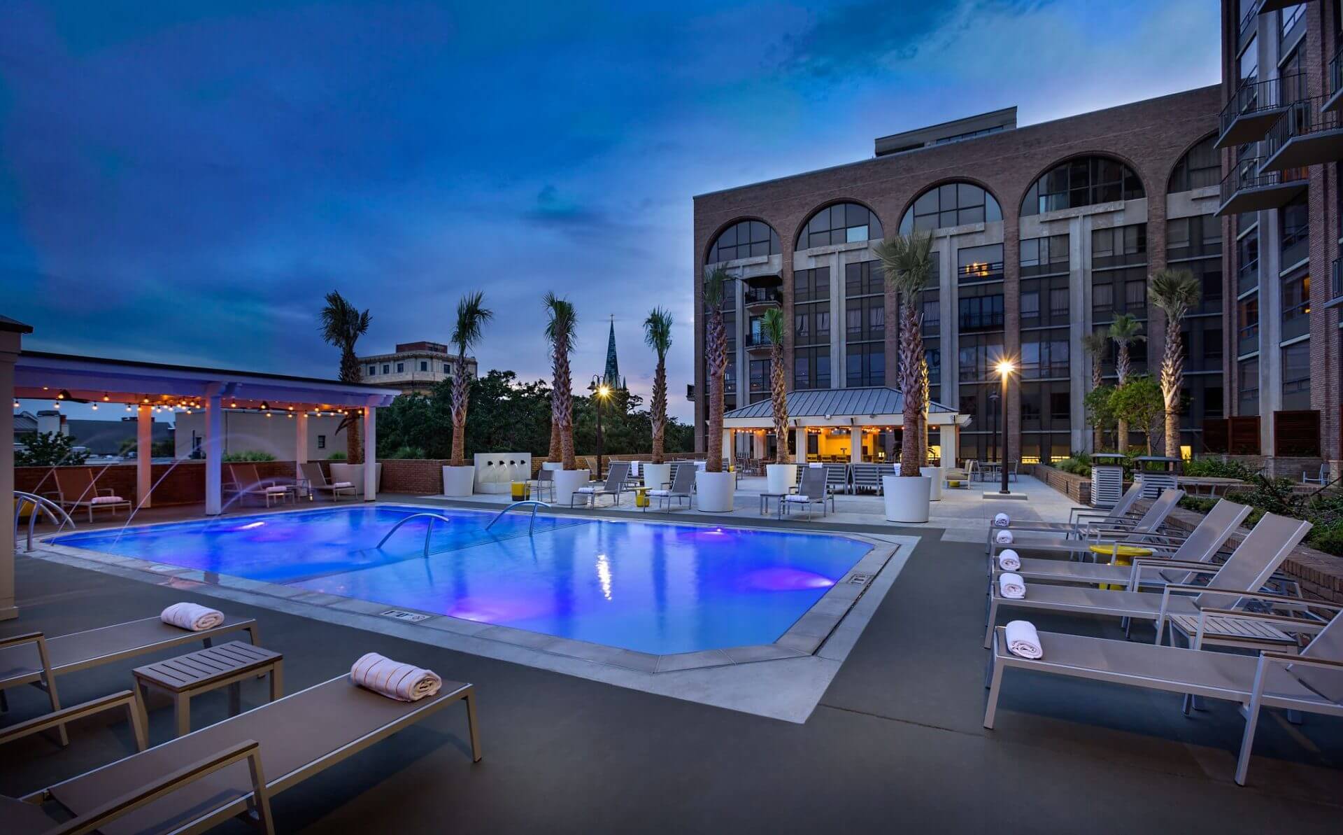 a pool with lounge chairs and palm trees in front of a building