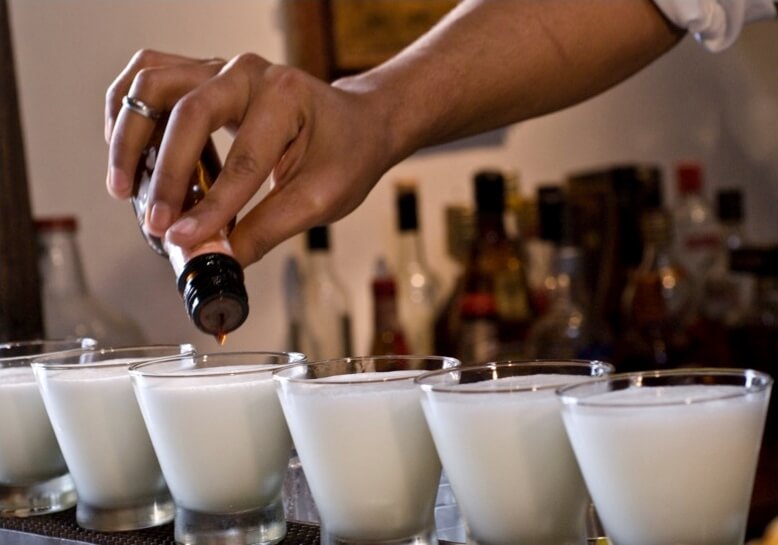 Bartender crafting white drinks and adding in bitters