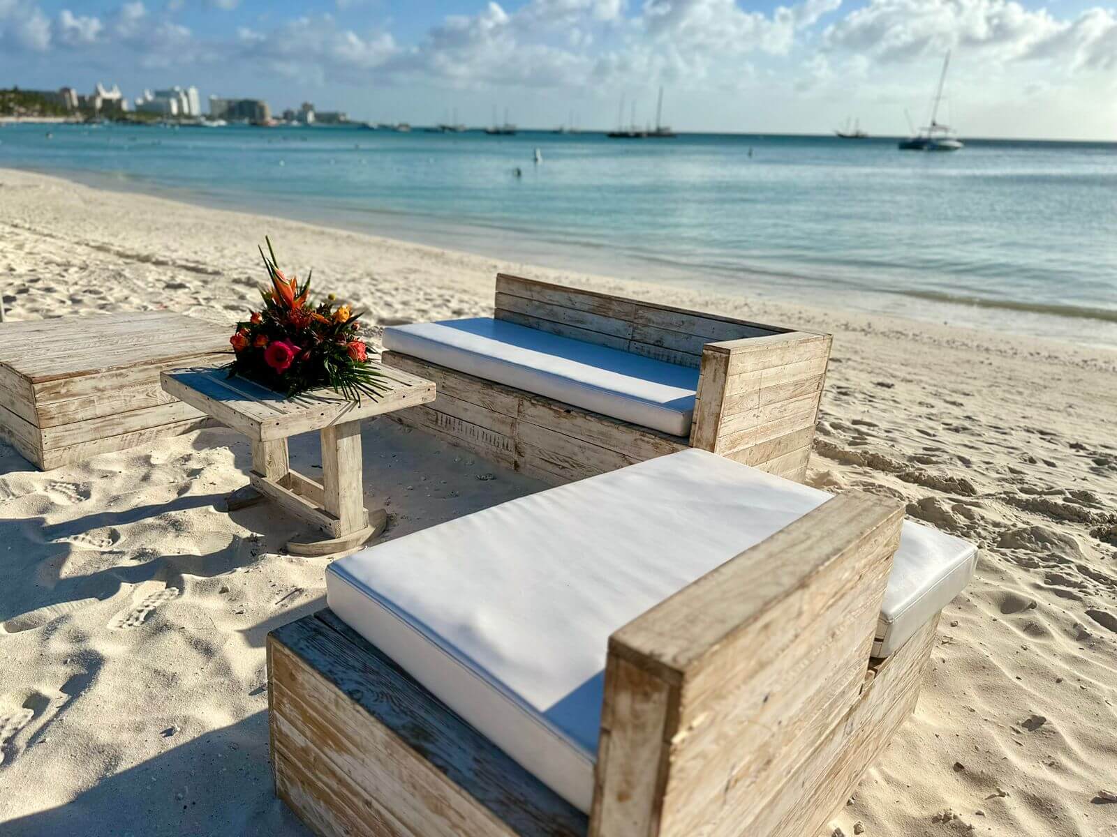 Whitewashed wooden couches with white cushions on beach in lounge set up