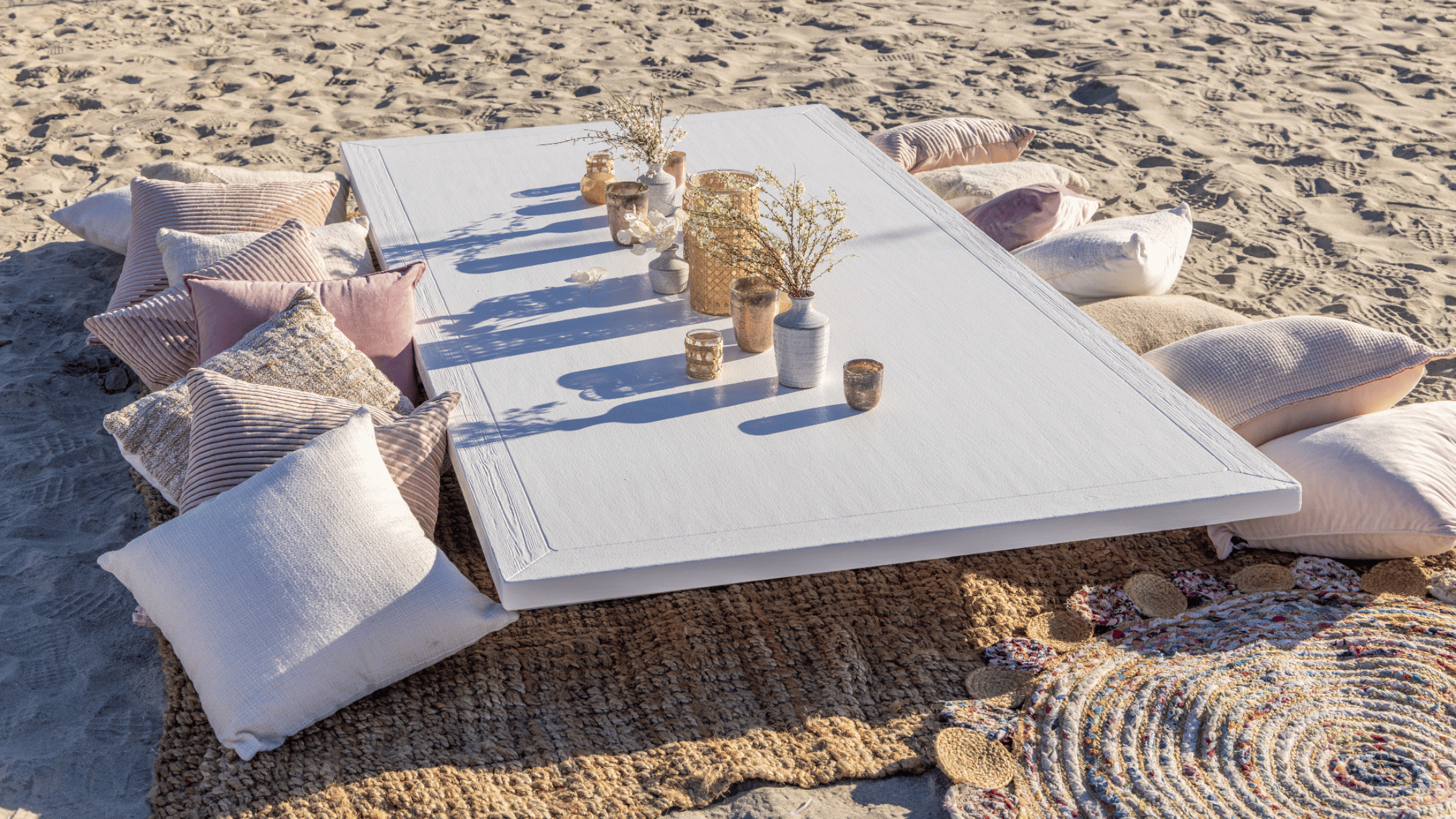 Beach picnic set up with pillow seats on sand and a low table on a textured beach blanket rug