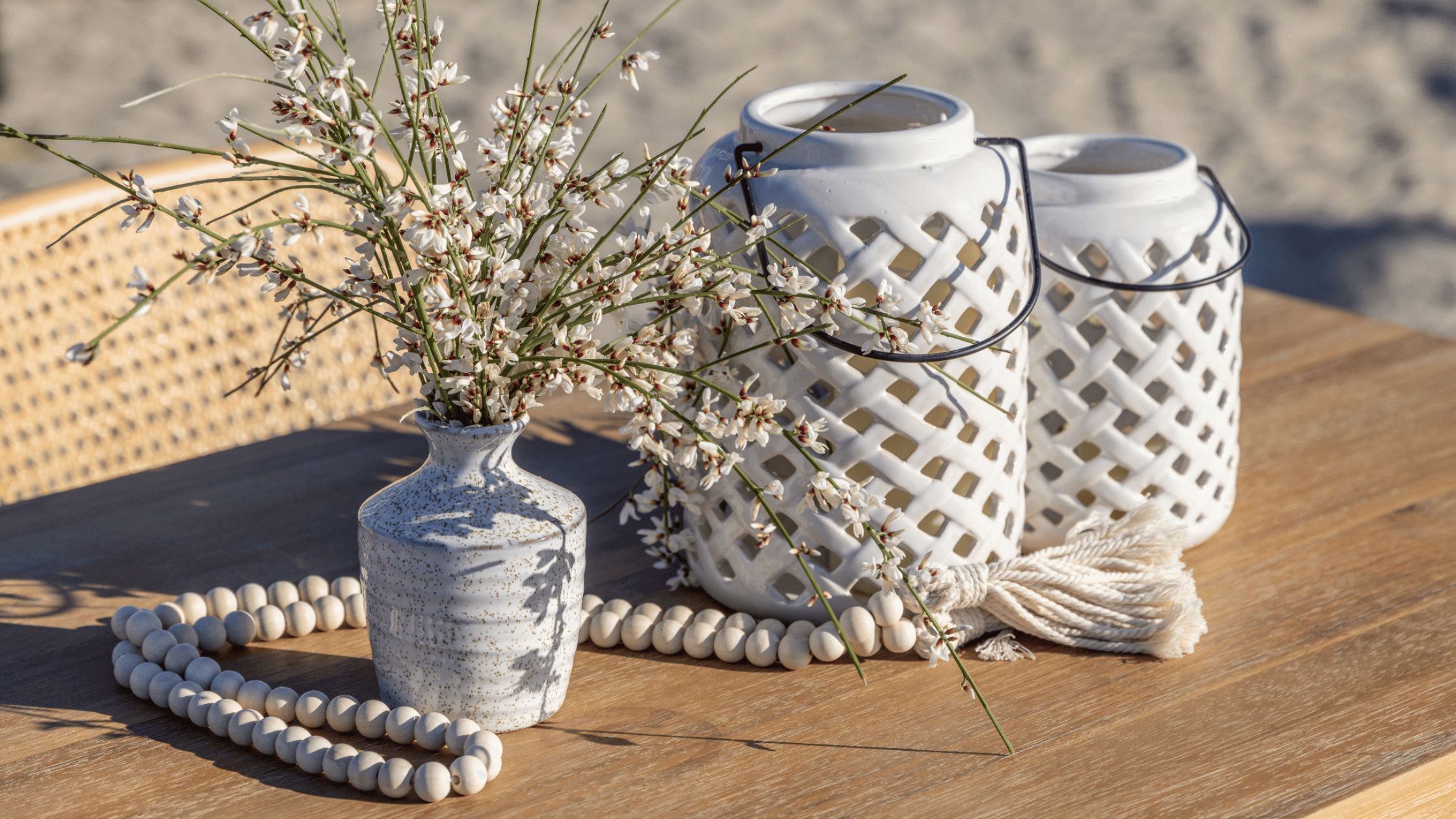 Coastal table decor with white ceramic lanterns and white clay vases with wild stems and wooden beads