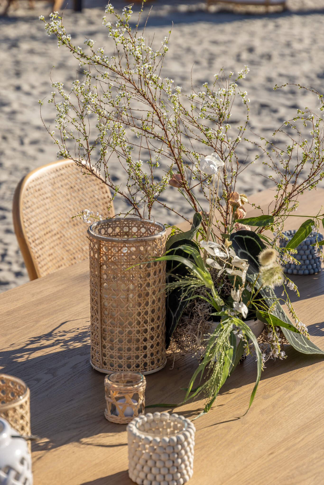 Coastal table decor with rattan hurricane and wood candle holders and a wild and beachy floral centerpiece