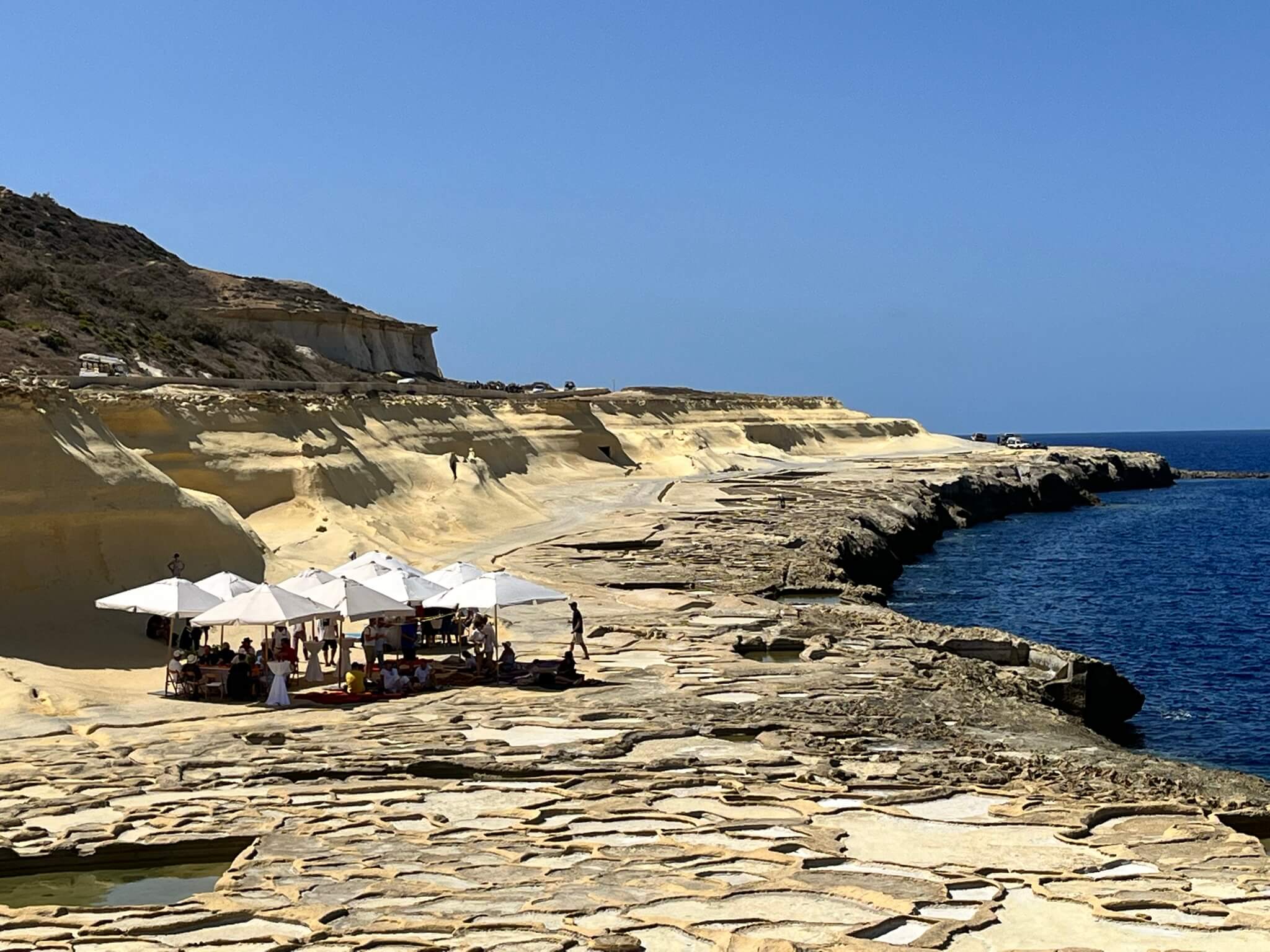 Beach set up with tables an d couches on Malta coast- zoomed out view with dunes, water and coastline view