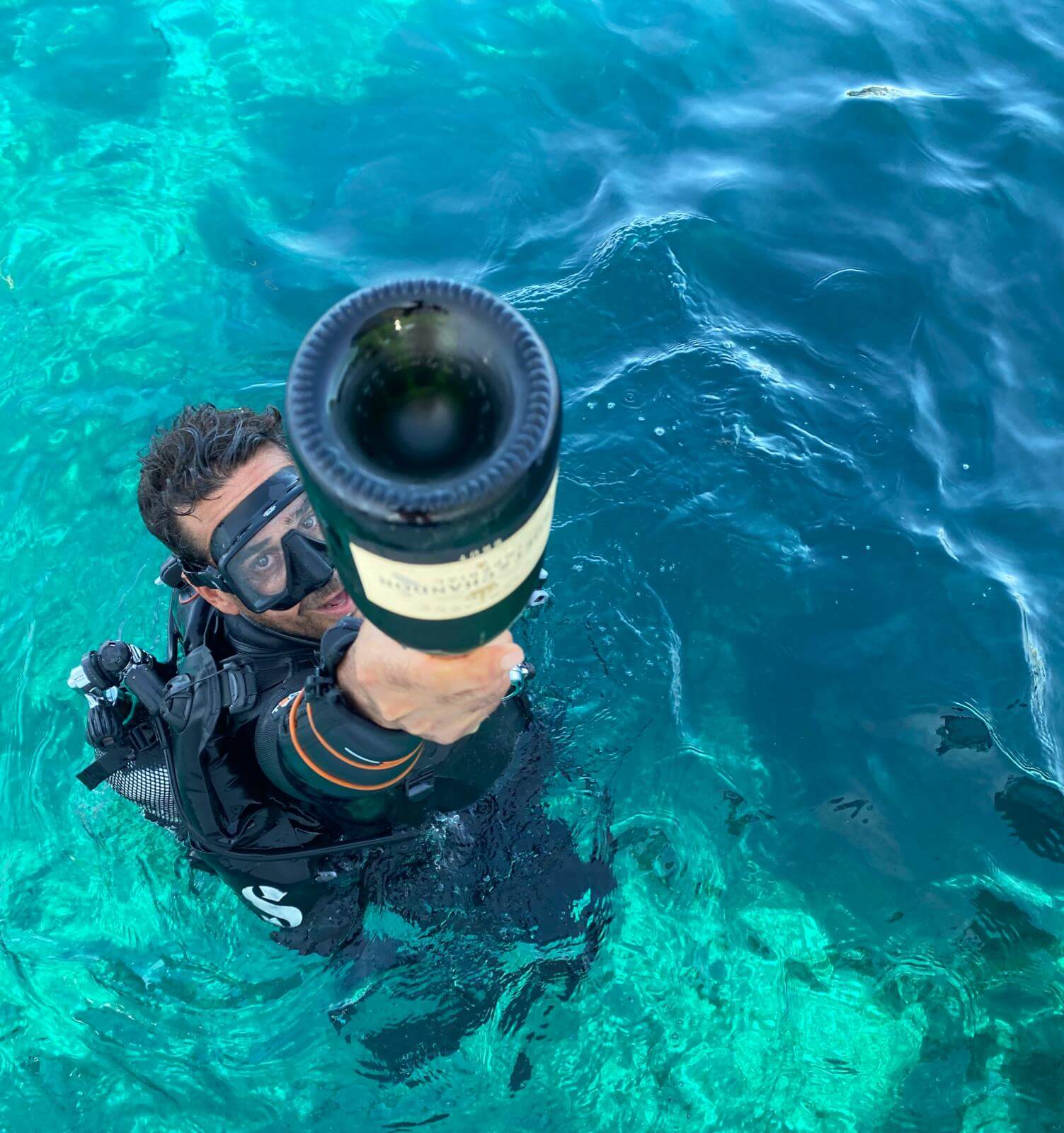 Maltese diver retrieving a bottle of champagne from the ocean floor where there is a wine cellar/crate that is perfectly chilled to the optimal temp with the oceans natural resources